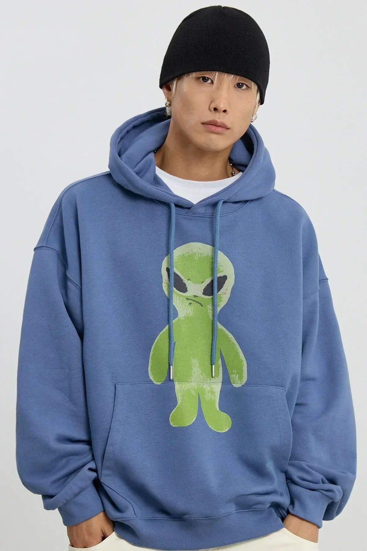 Young man wearing dust blue hoodie with green alien graphic and black beanie against white background