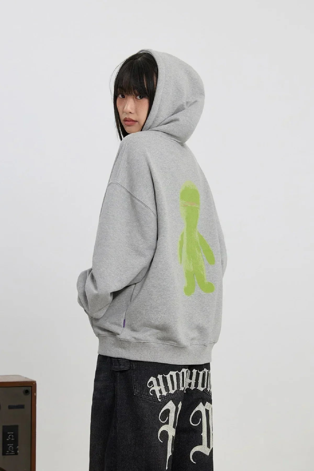 Young woman wearing grey alien graphic hoodie with green figure print on back and black graphic skirt