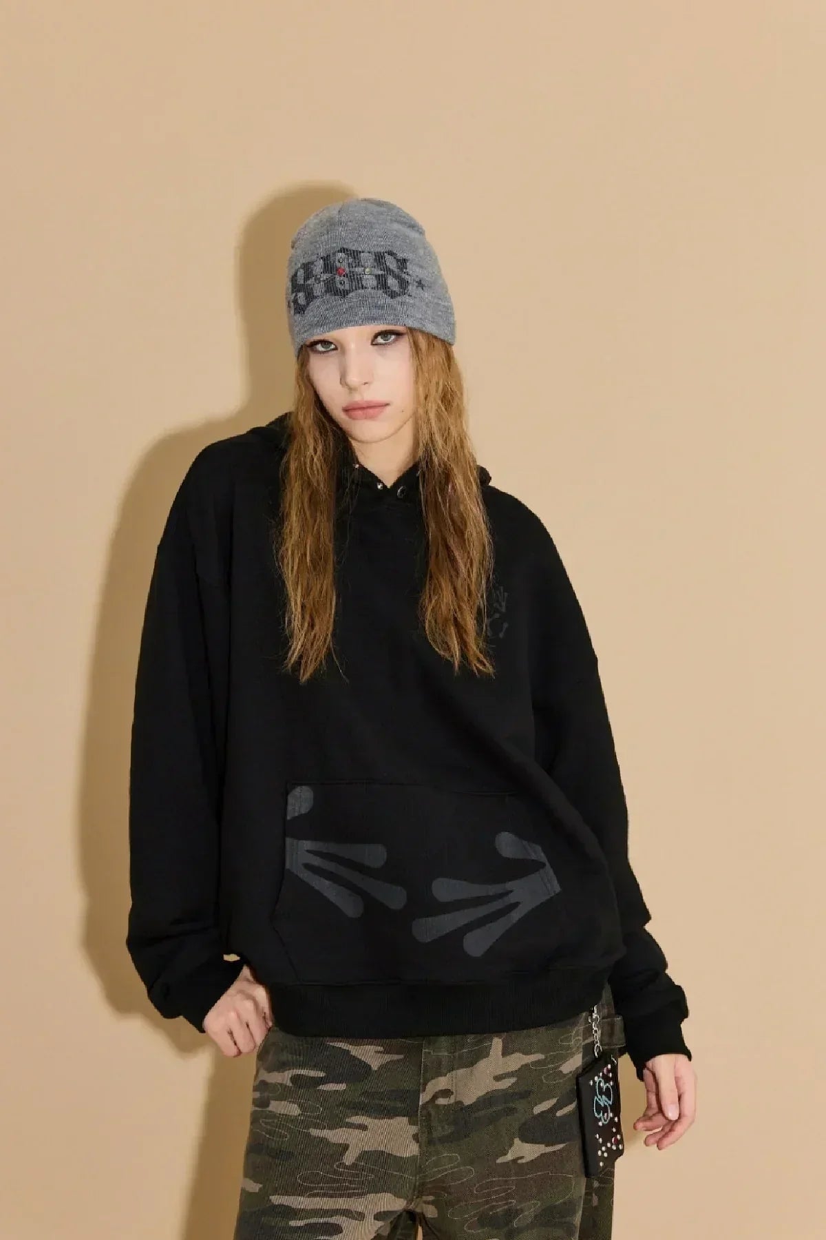 Model wearing black hoodie with alien hands design and camo pants, styled with gray graphic beanie