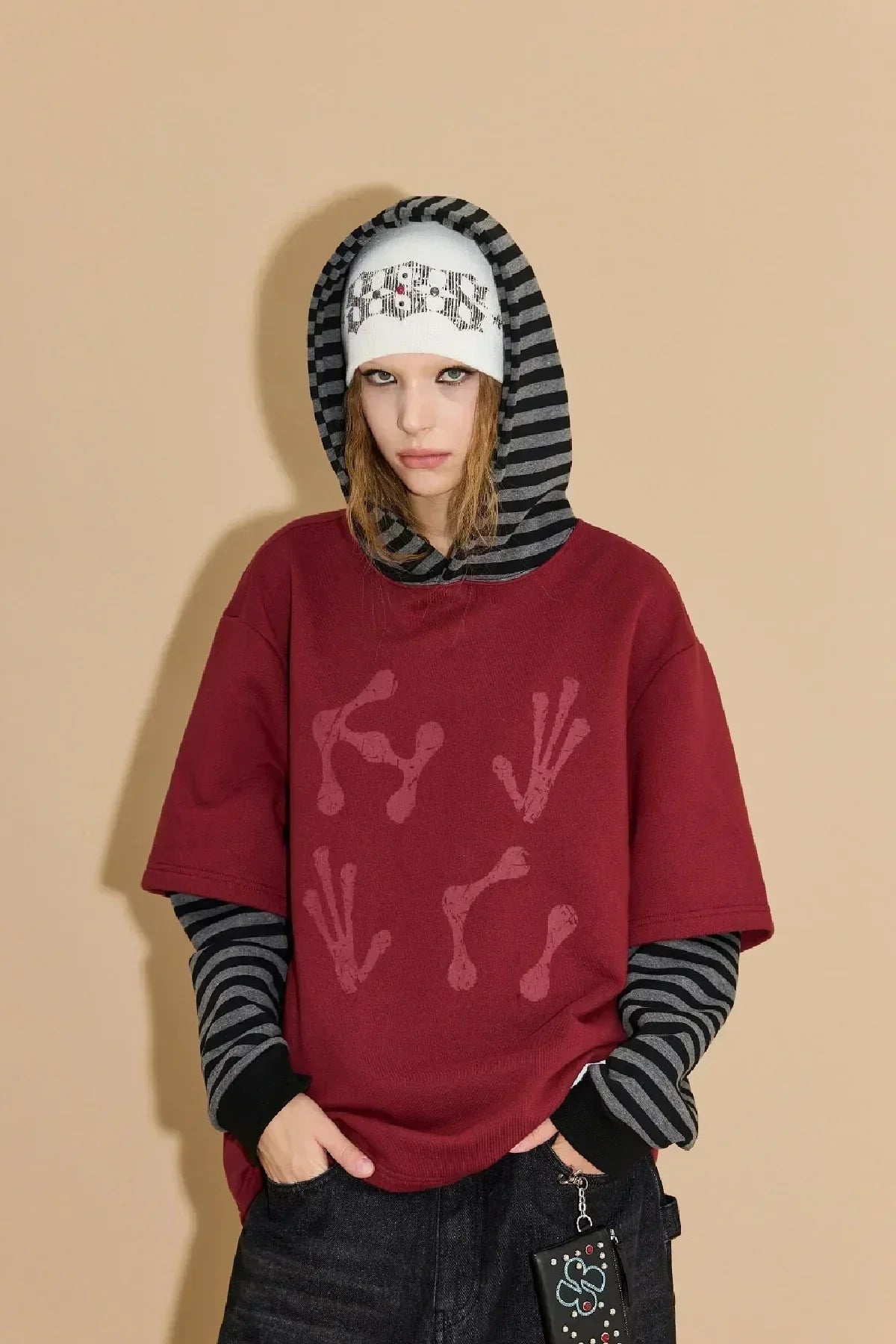 Young woman wearing burgundy short-sleeve hoodie with red abstract print and black-gray striped long sleeves