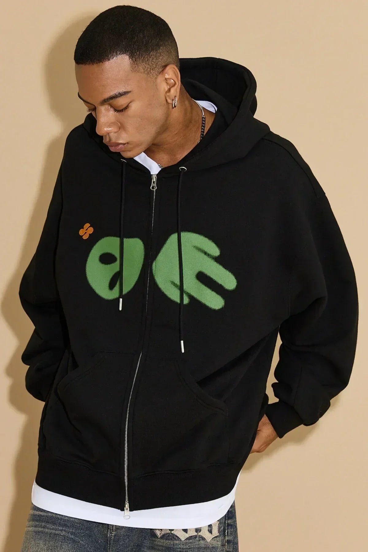 Young man wearing black zip-up hoodie with green alien graphic and orange detail on chest