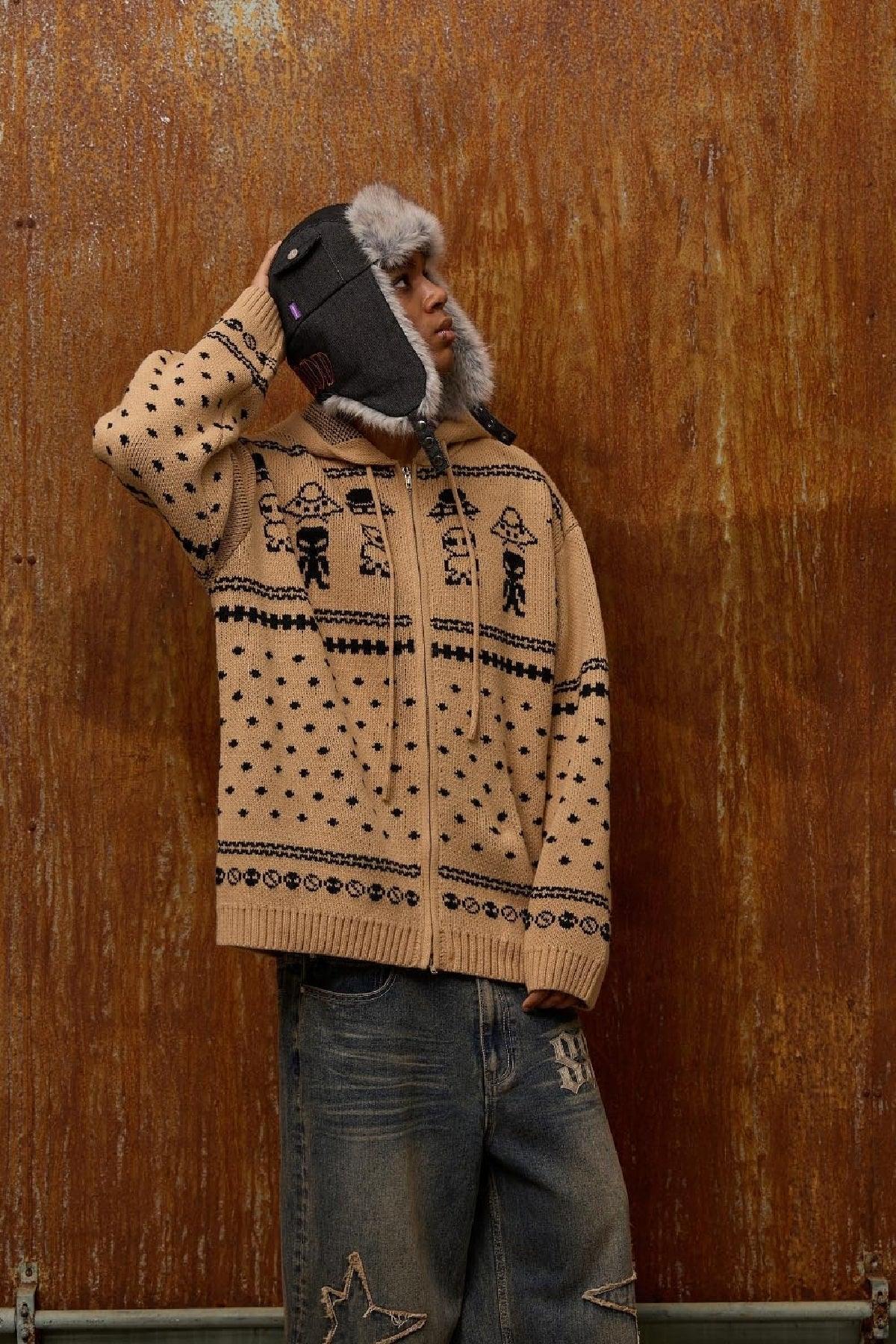 Person wearing beige alien pattern knit zip-up hoodie and fur-trimmed winter hat against rusty wall