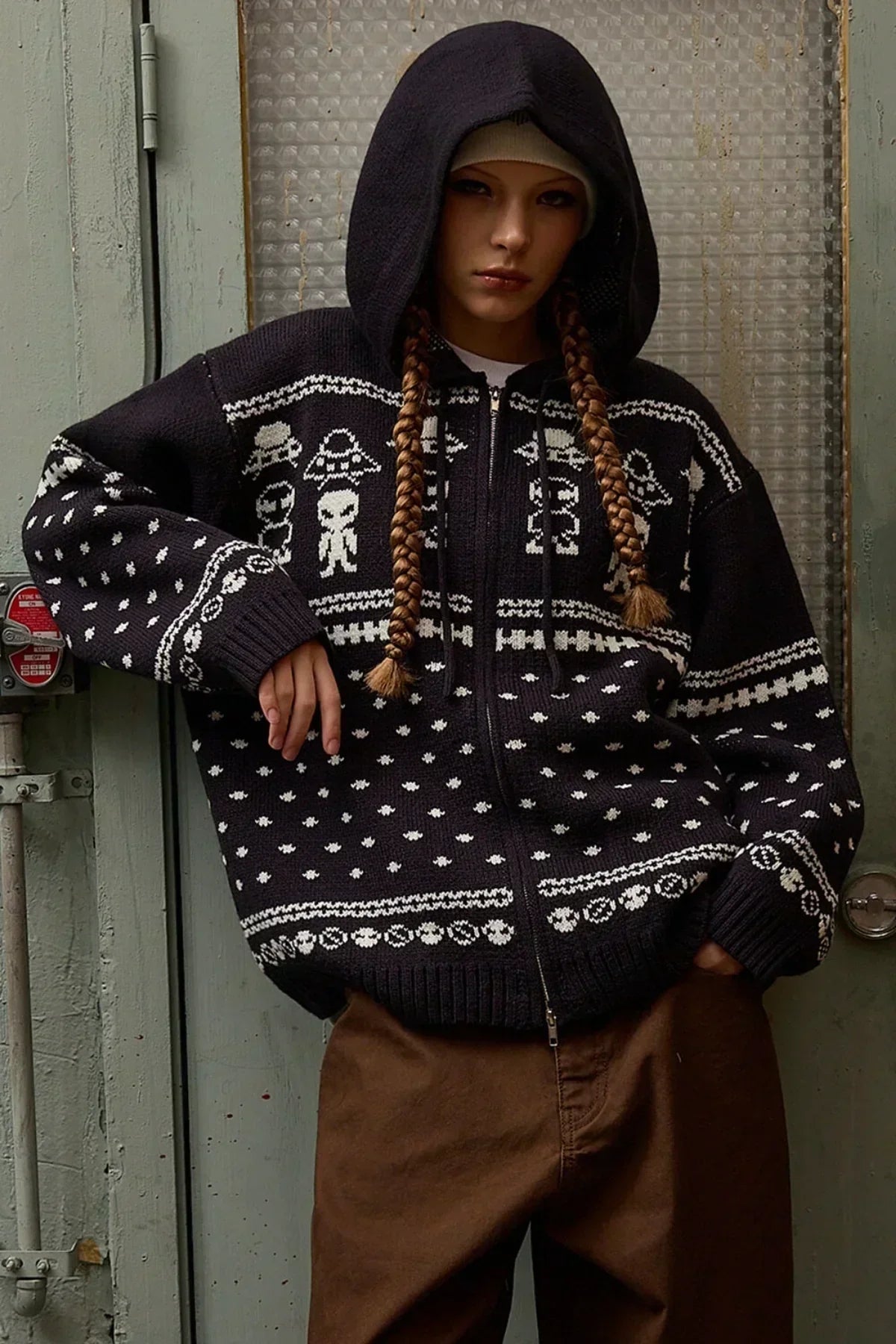 Woman wearing navy knit zip-up hoodie with white alien pattern and brown pants