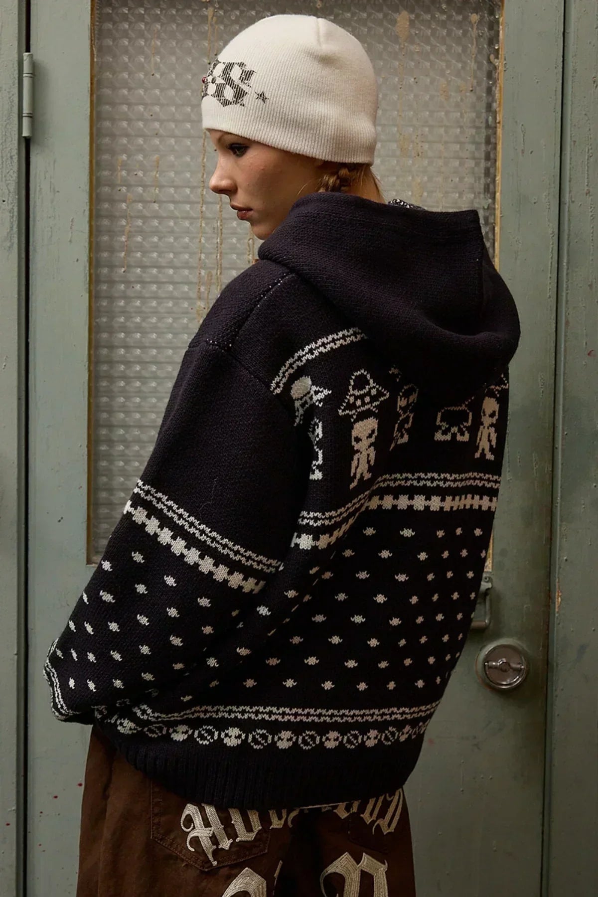 Side view of a person wearing a navy knit hoodie with white alien pattern and a white beanie hat
