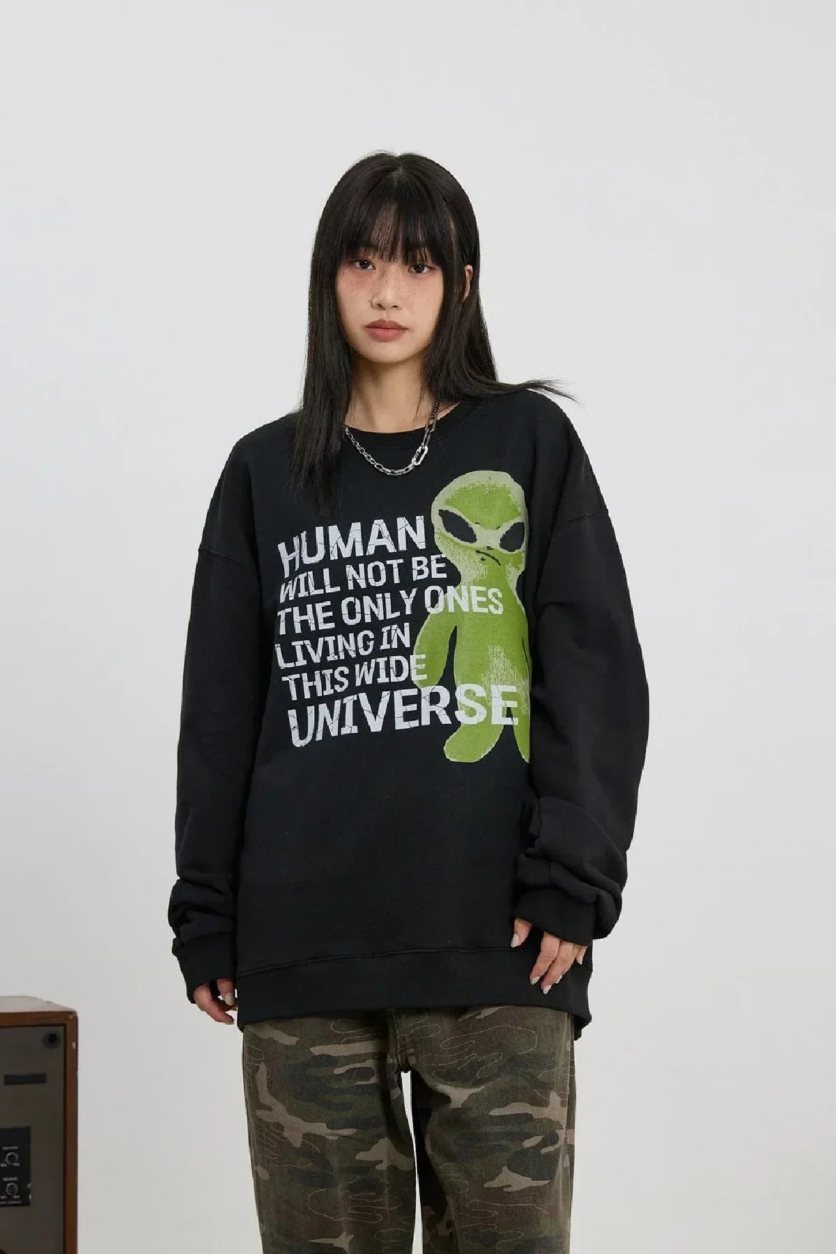 Woman wearing black sweatshirt with green alien graphic and text, paired with camouflage pants