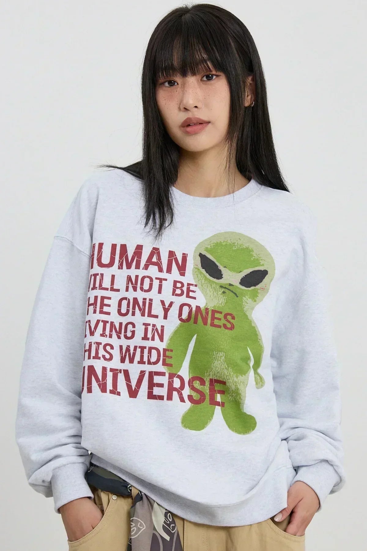 Asian woman wearing a light grey sweatshirt with a green alien graphic and red slogan text