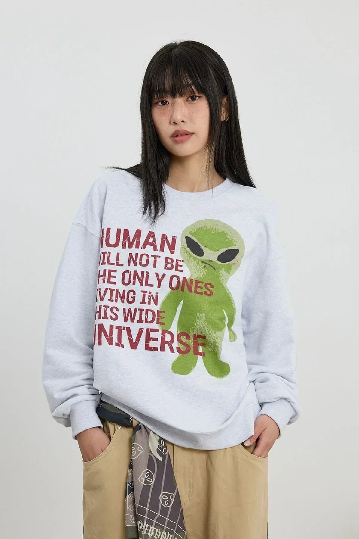 Young woman wearing gray alien slogan sweatshirt with green alien graphic and red text