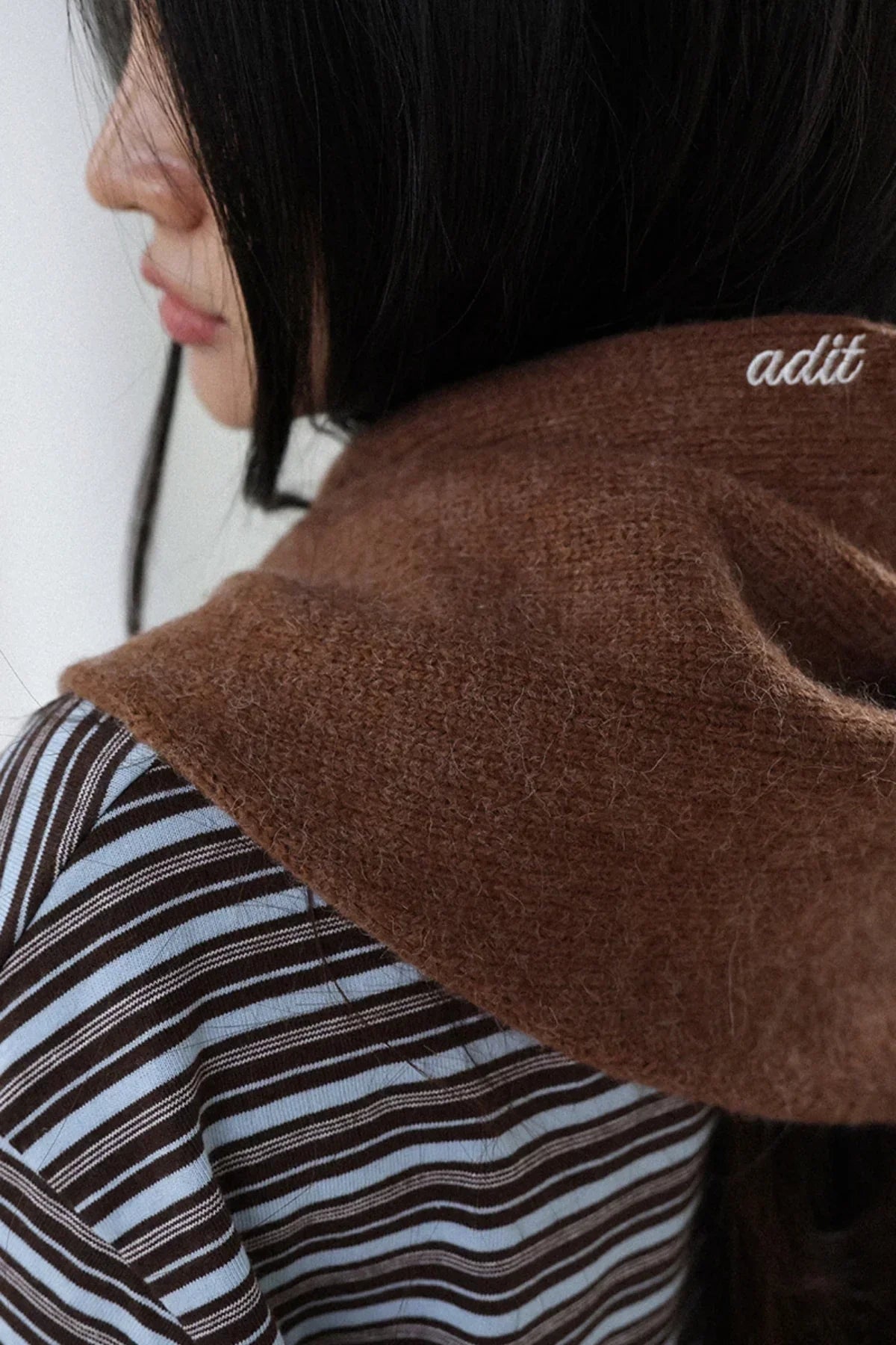 Close-up of woman wearing brown alpaca muffler over striped shirt with 'adit' embroidery