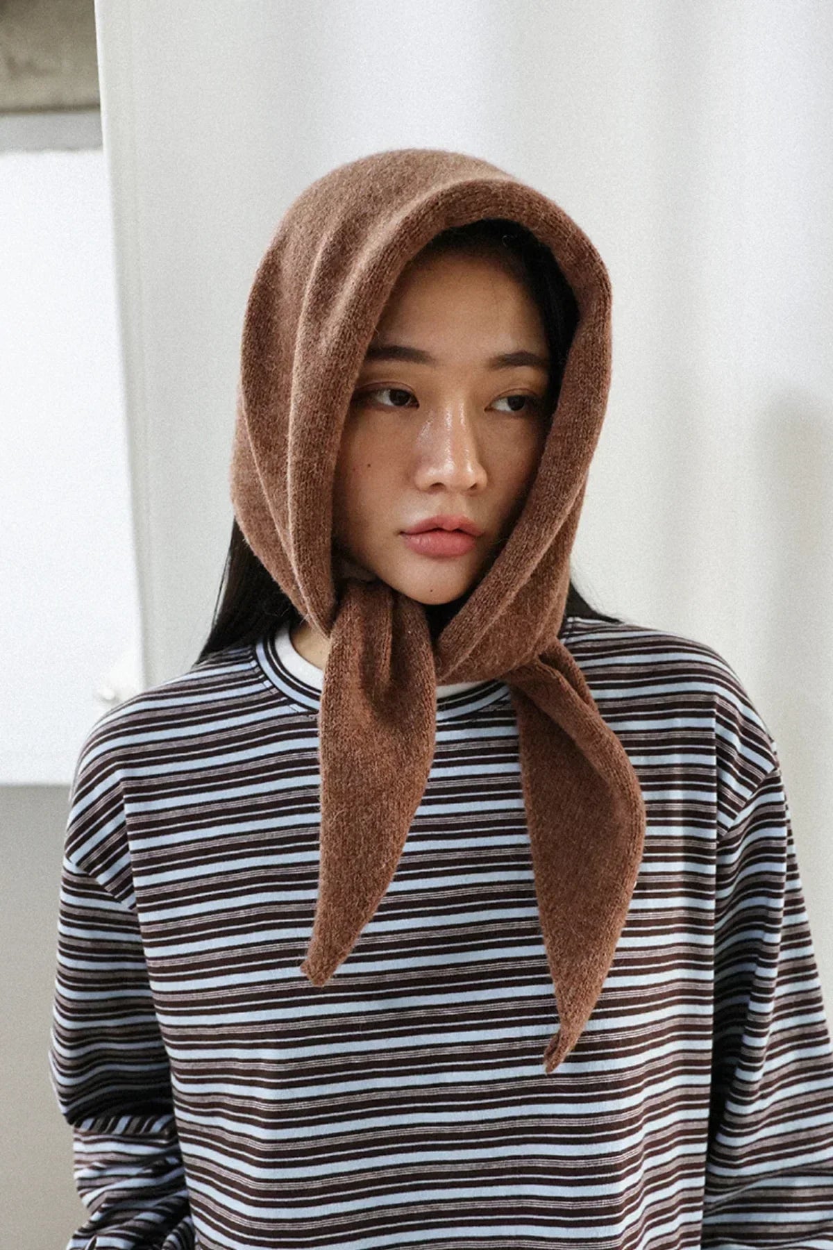 Portrait of woman wearing brown alpaca wool scarf tied around head and striped shirt indoors