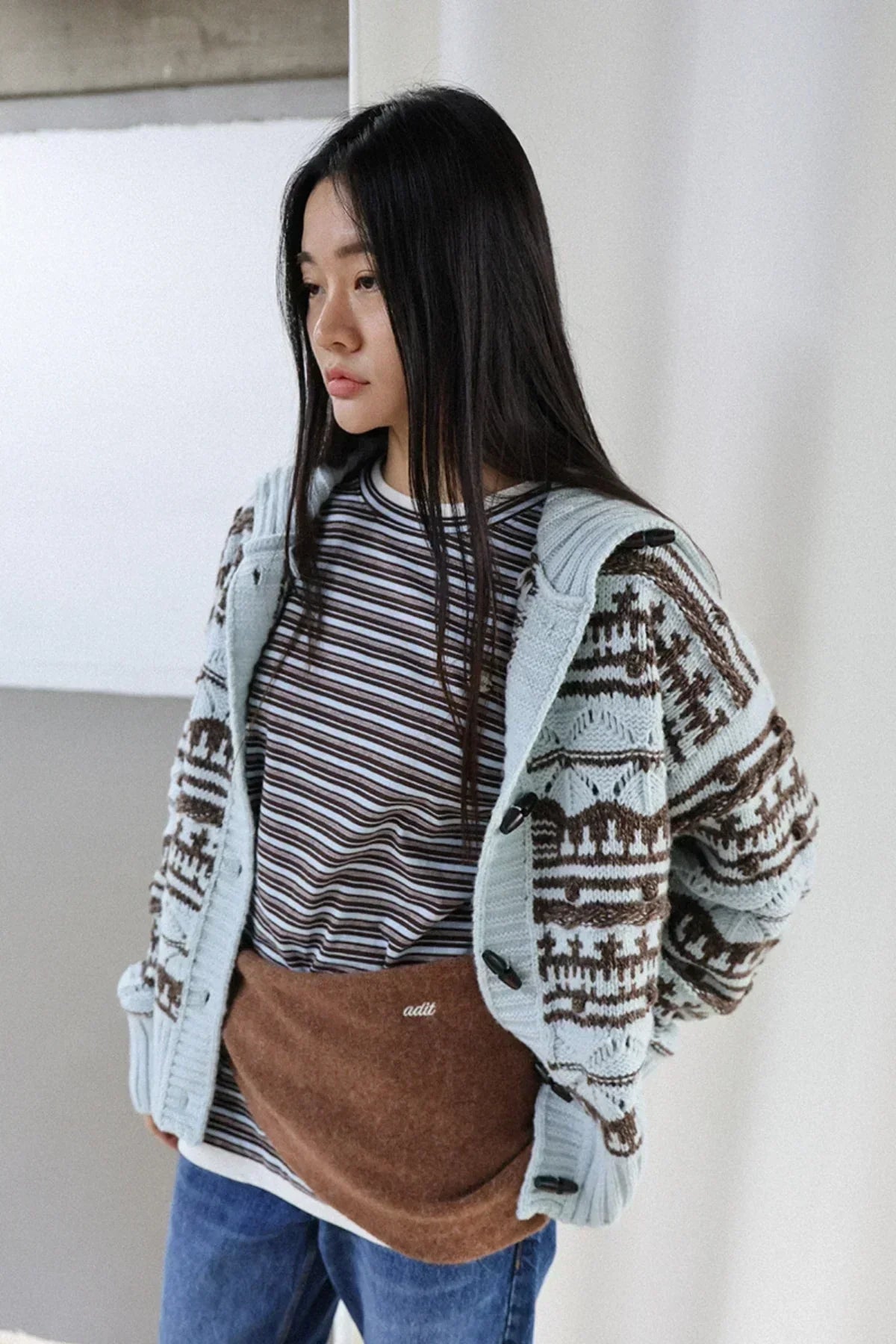 Woman wearing brown alpaca multi muffler, patterned cardigan, striped shirt, and blue jeans in studio