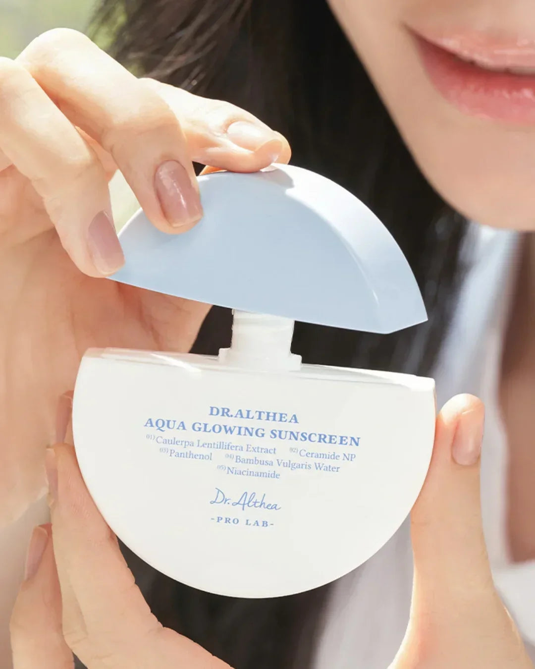 Close-up of a woman holding Dr.Althea Aqua Glowing Sunscreen bottle with light blue cap