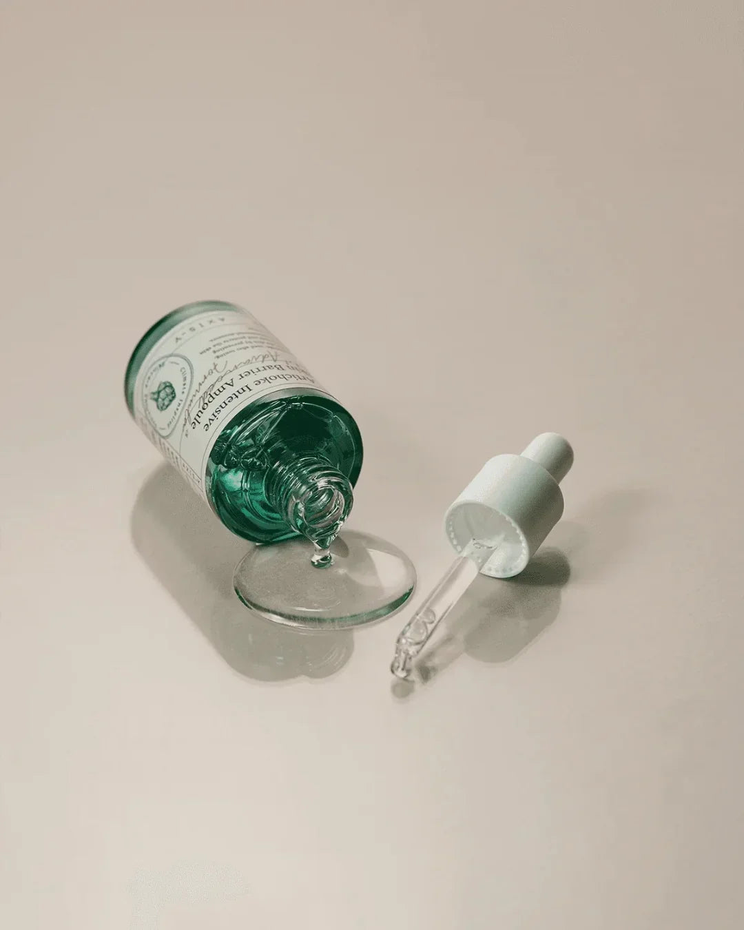 Artichoke Intensive Skin Barrier Ampoule bottle spilling clear serum with dropper on beige surface