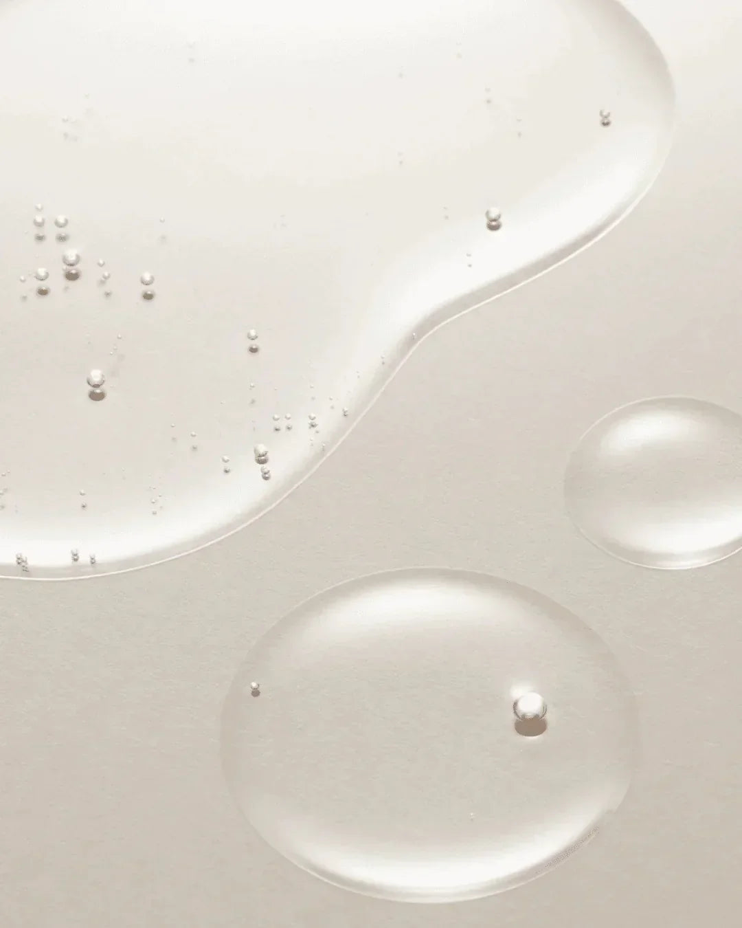 Clear skincare serum drops with tiny air bubbles on a light neutral background