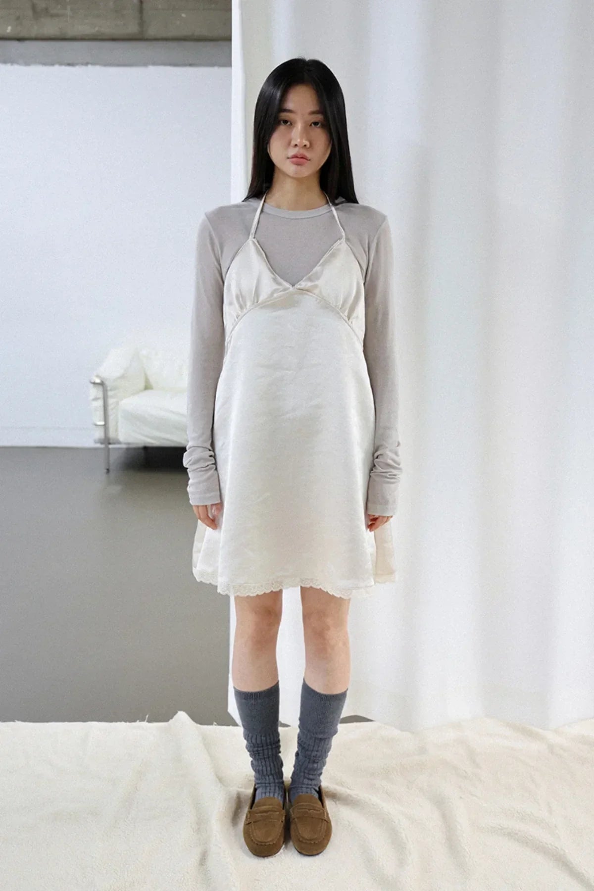 Model wearing beige satin slip dress layered over long sleeve top with gray socks and brown loafers