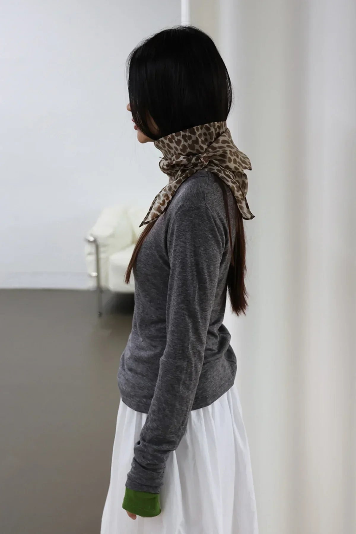 Woman in charcoal long sleeve top and leopard print scarf, side view in minimal indoor setting