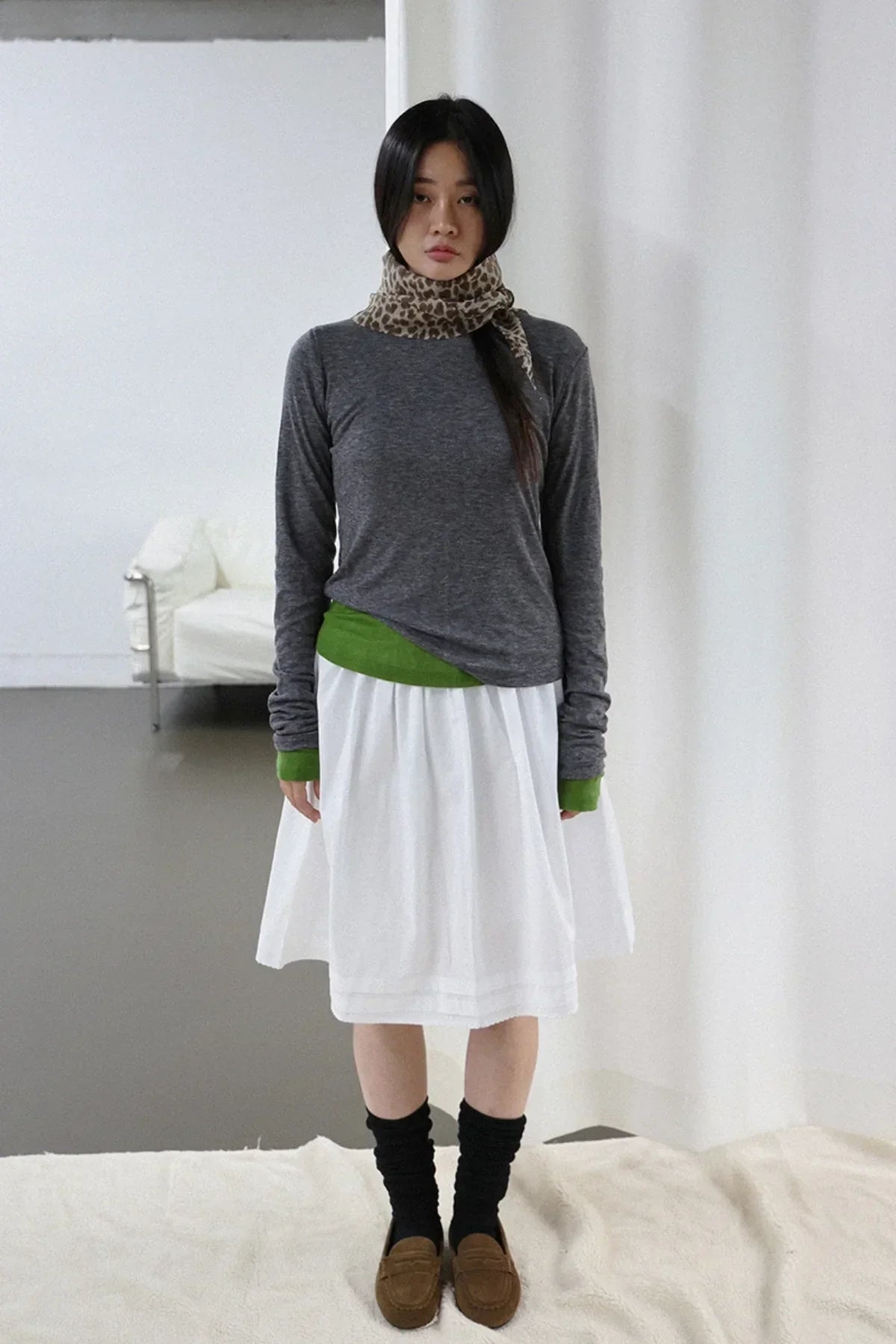 Woman wearing charcoal long sleeve top with green cuffs, white skirt, leopard print scarf, black socks, and brown loafers