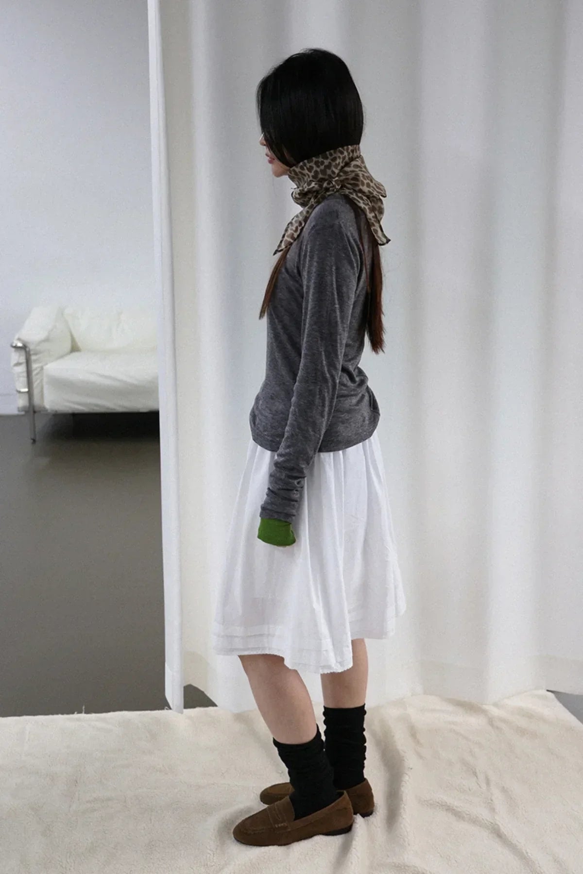Side profile of woman wearing charcoal long-sleeve top, white skirt, leopard print scarf, black socks, and brown loafers