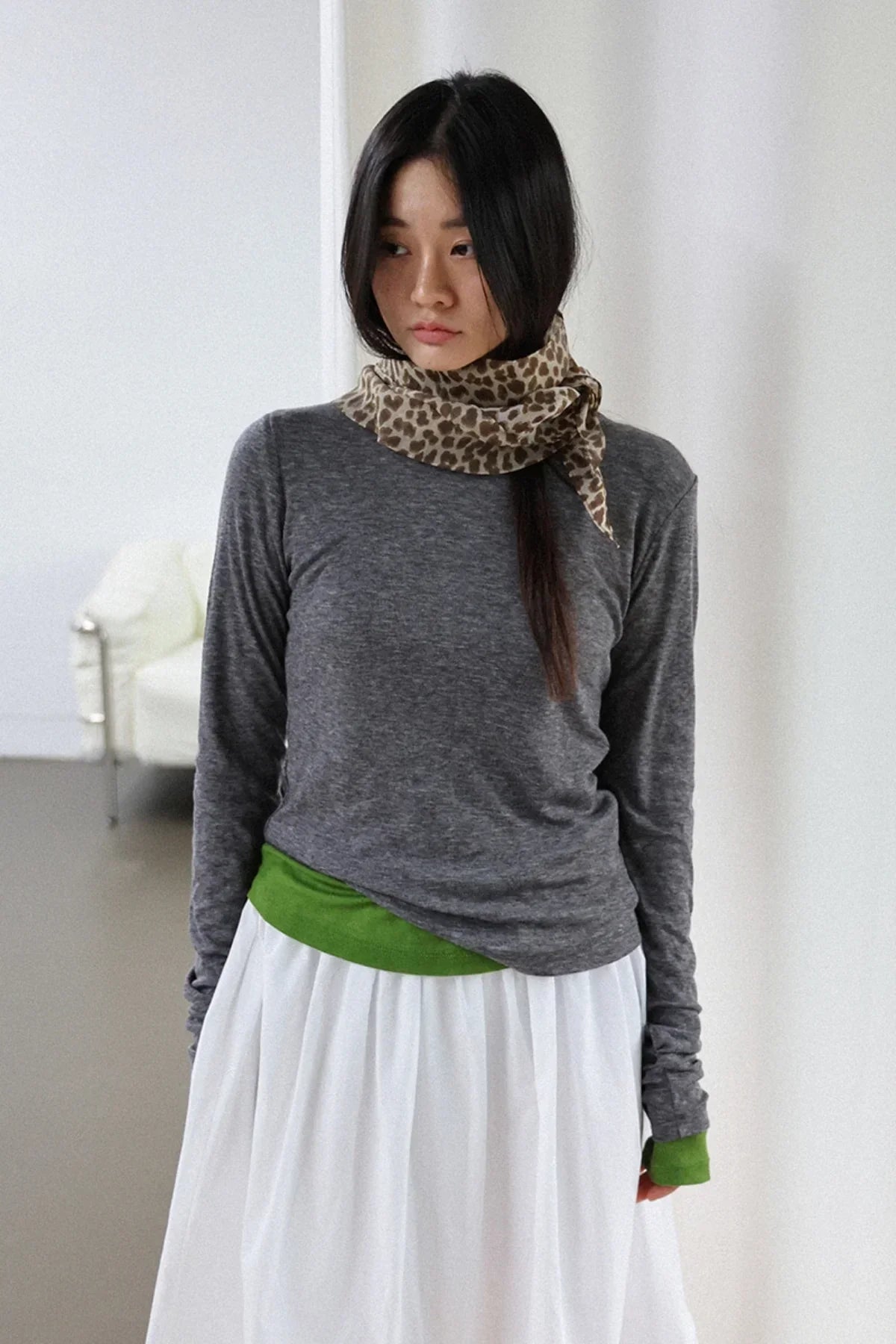Woman wearing charcoal gray long sleeve top with green cuffs and leopard print scarf in minimal white room