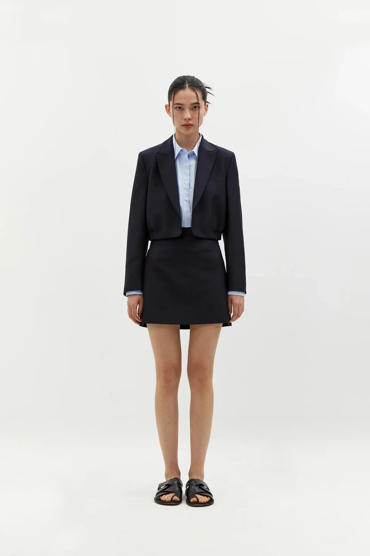 Woman wearing navy cropped blazer and matching mini skirt with light blue shirt and black sandals