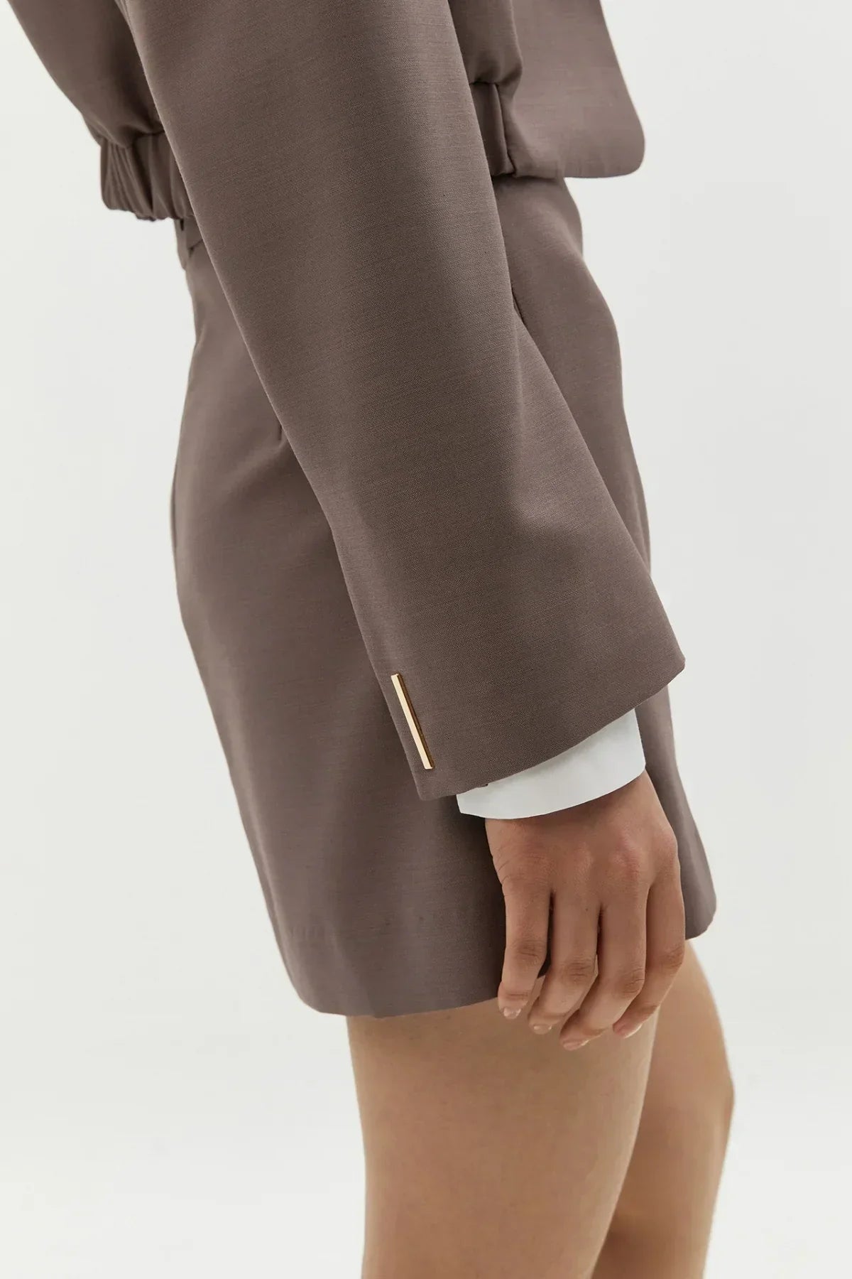 Close-up of a woman's hand wearing a taupe skirt suit with a gold bar detail on the sleeve cuff