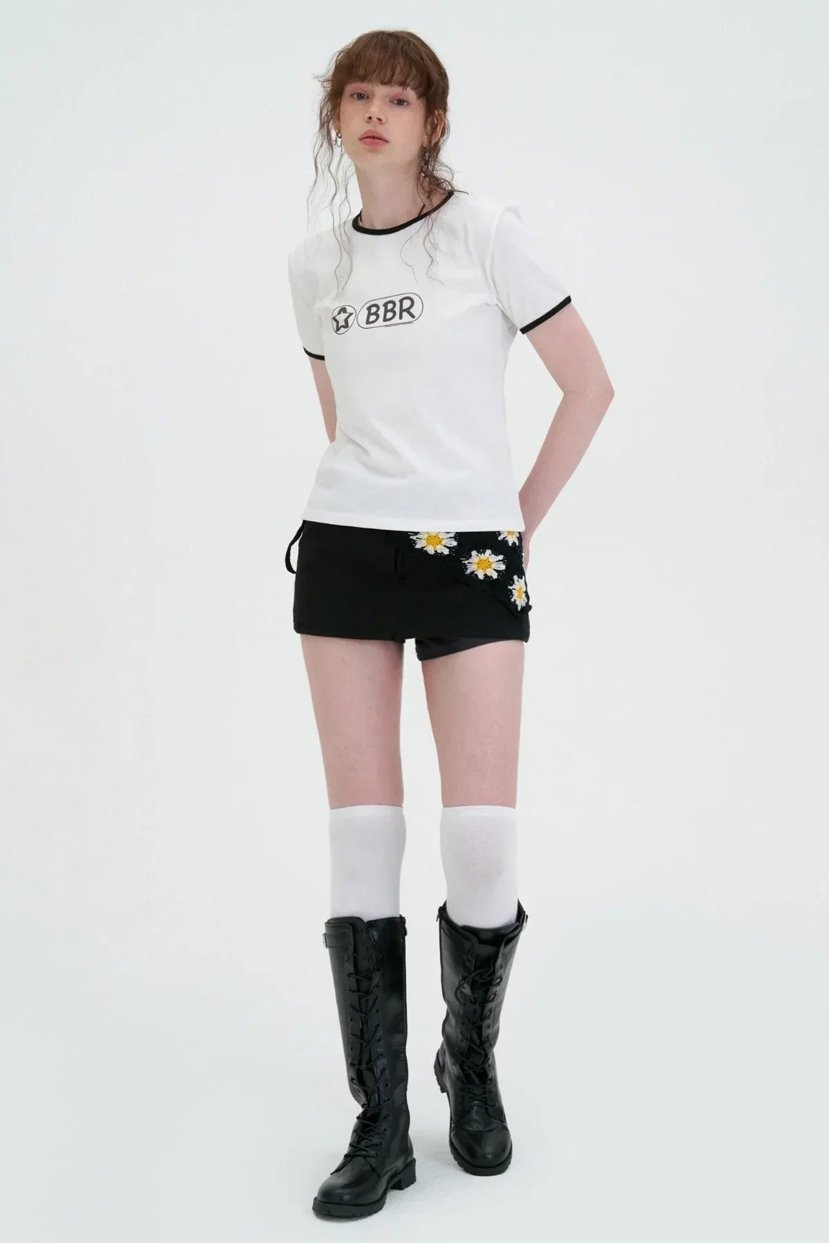 Young woman wearing white BBR logo t-shirt, black floral mini skirt, white knee socks, and black lace-up boots