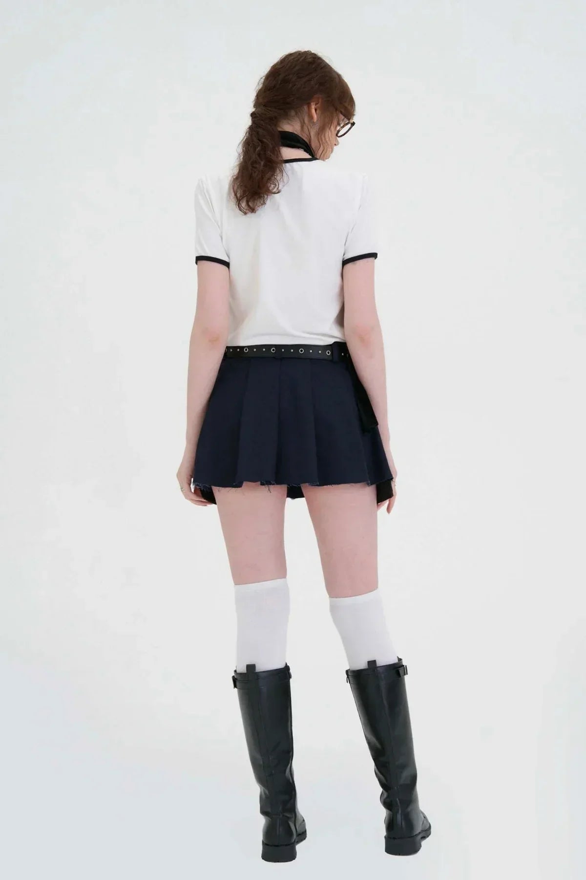 Back view of woman wearing white t-shirt, navy pleated mini skirt, white knee socks, and black boots