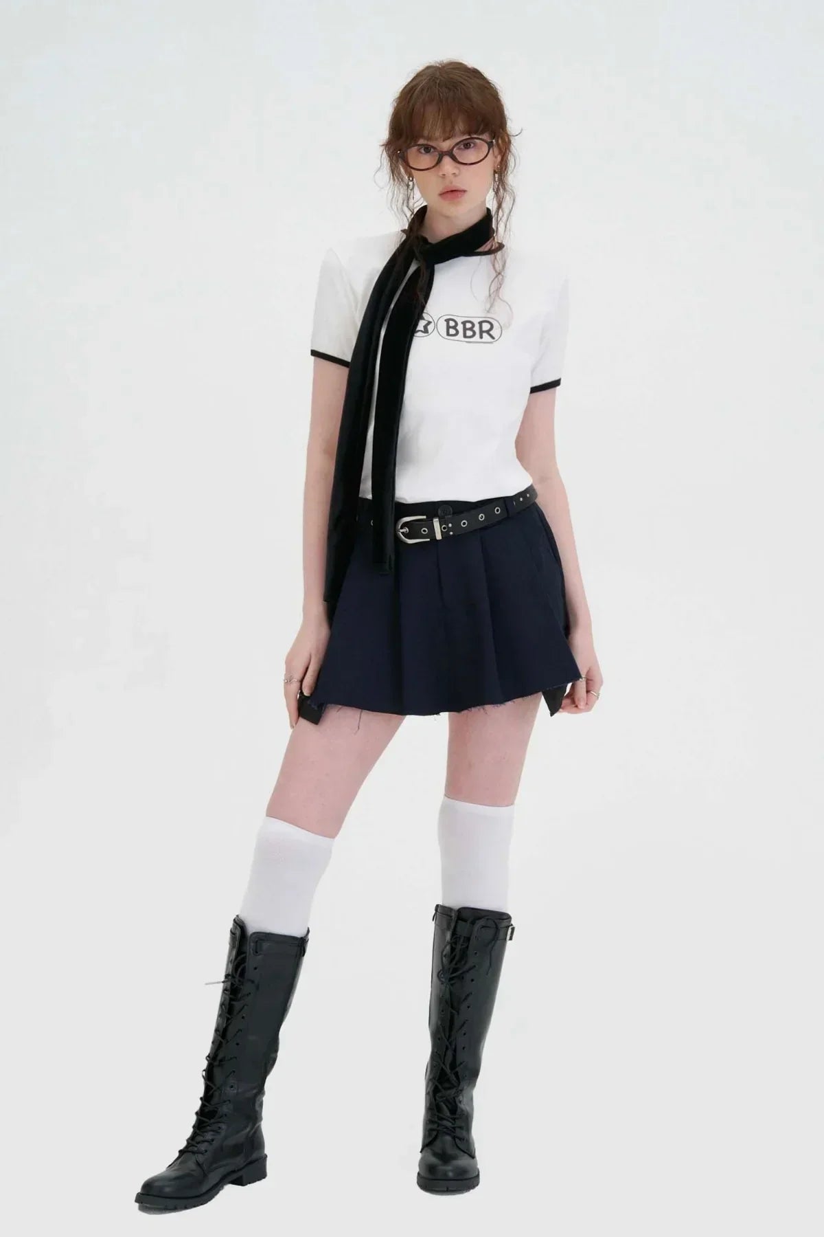 Young woman wearing white BBR logo t-shirt, navy mini skirt, black belt, knee-high boots, and glasses