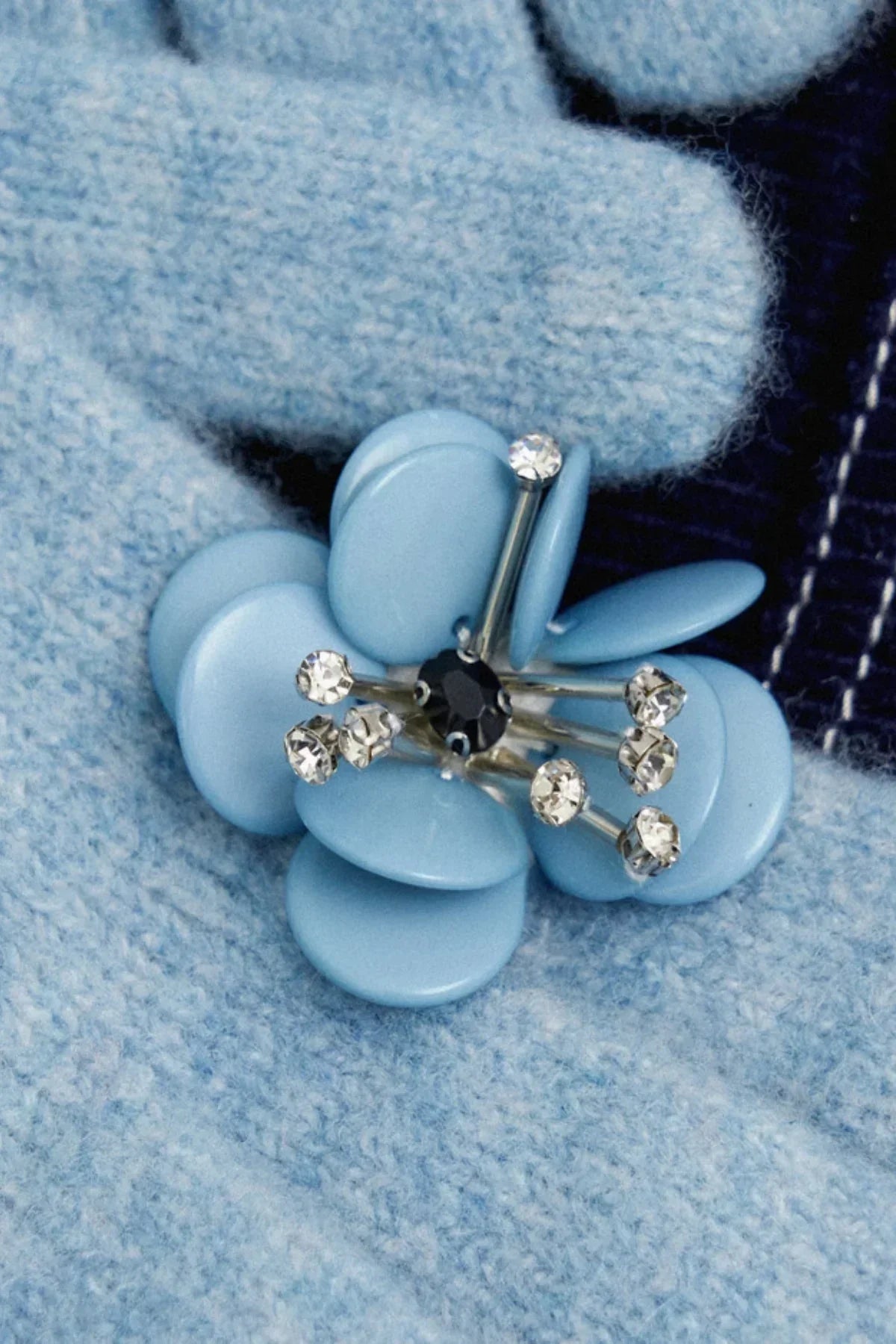 Close-up of a blue floral ring with beads and rhinestones on a knitted blue fabric