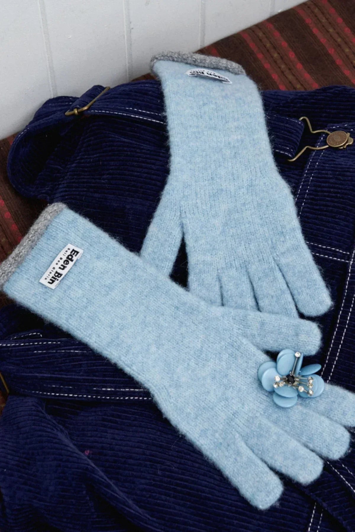 Light blue wool gloves with grey trim and flower brooch on navy blue corduroy jacket