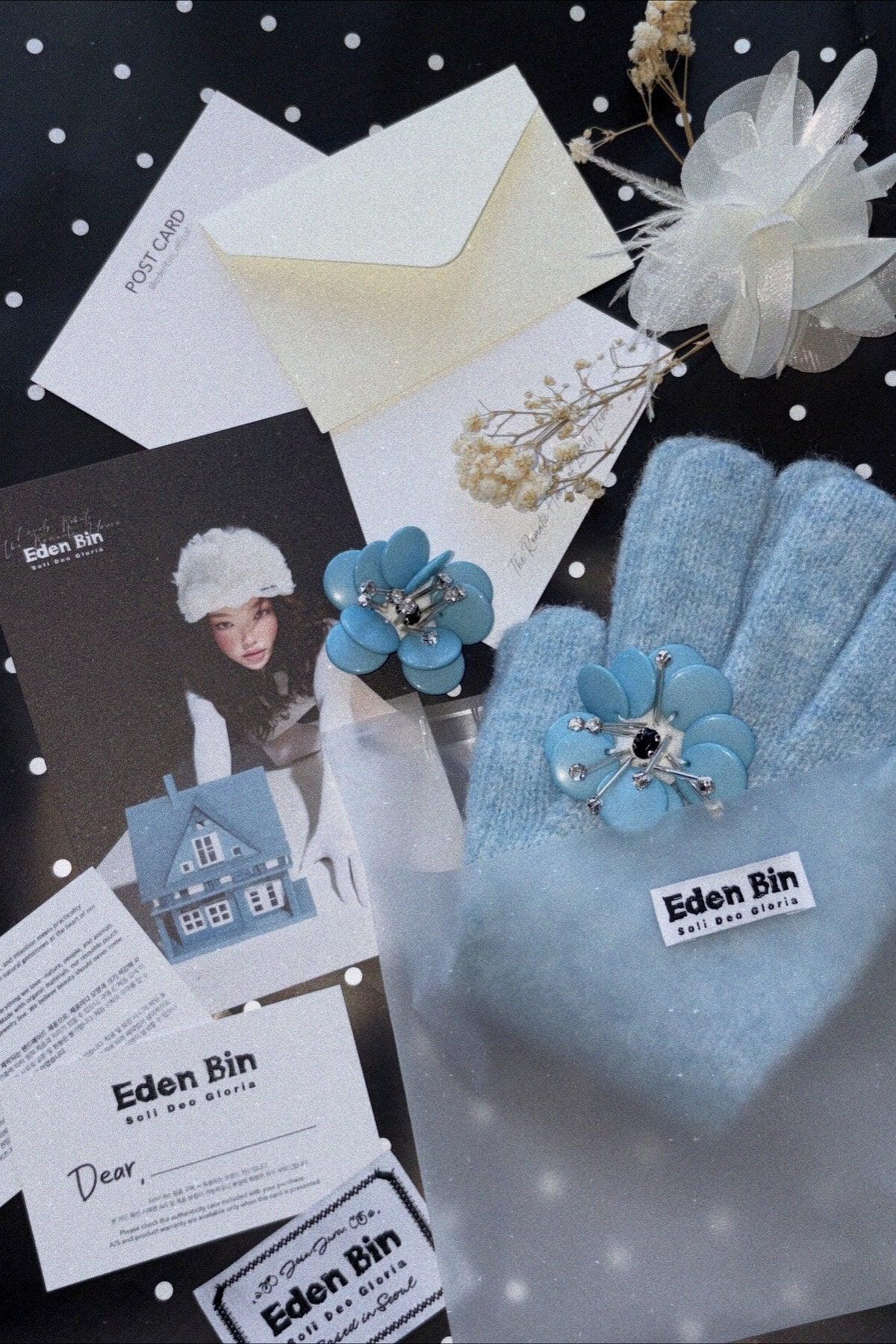 Light blue knitted gloves with floral jewel rings on black polka dot background with Eden Bin branding cards and white decorative flower