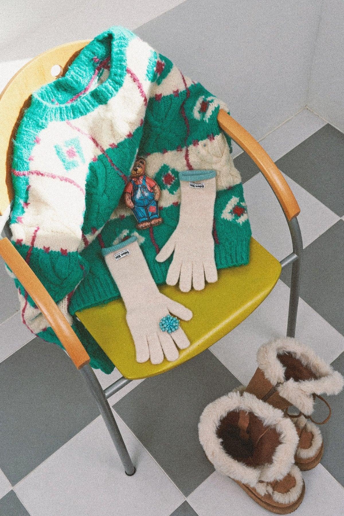 Green and white patterned sweater on yellow chair with cream gloves and brown fur-lined boots