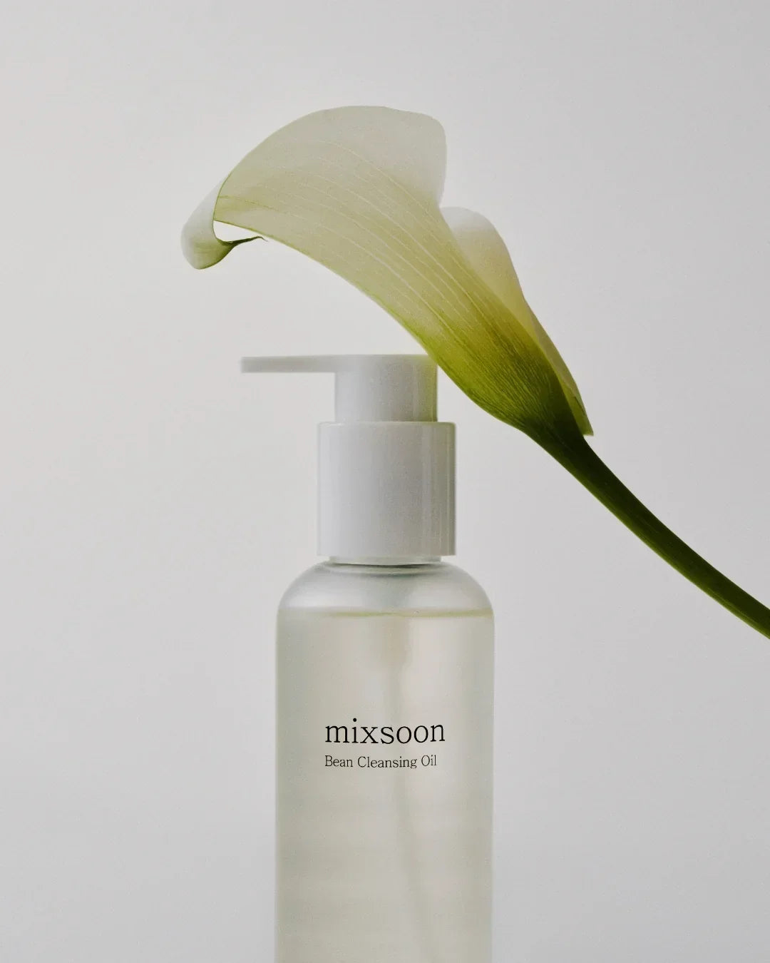 Mixsoon Bean Cleansing Oil bottle with white calla lily flower on plain background