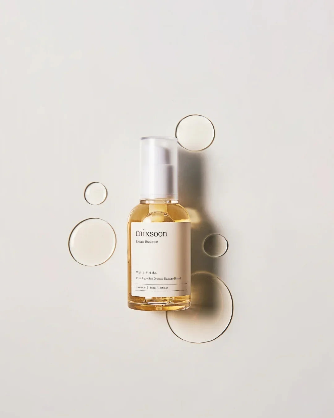 Mixsoon Bean Essence skincare serum in a clear pump bottle with oil droplets on light background