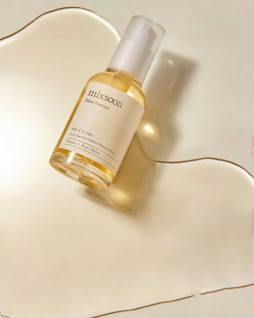 Mixsoon Bean Essence skincare bottle with yellow liquid on beige background and liquid spill