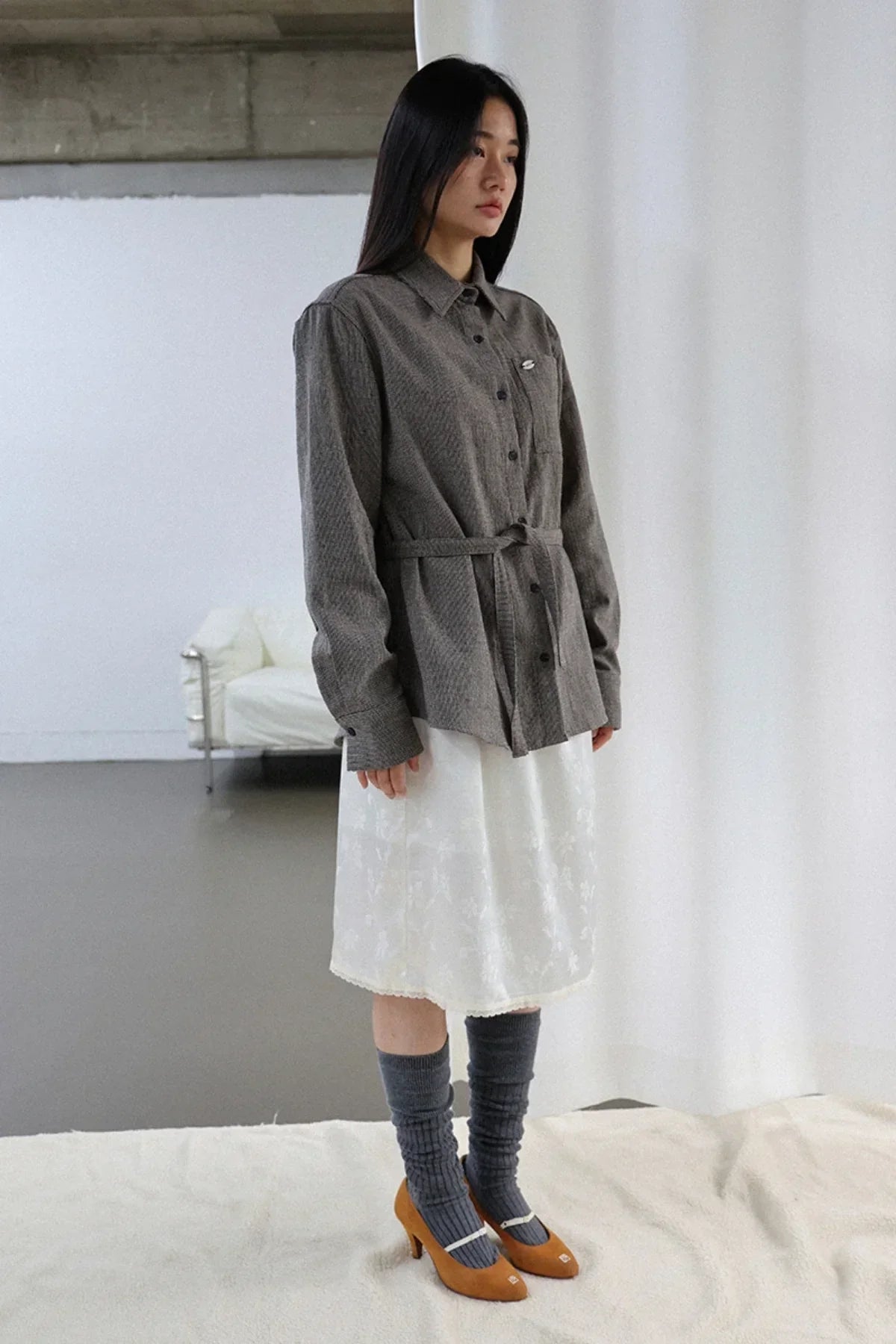 Model wearing a gray belted shirt jacket with white floral skirt and gray knee-high socks with brown heels