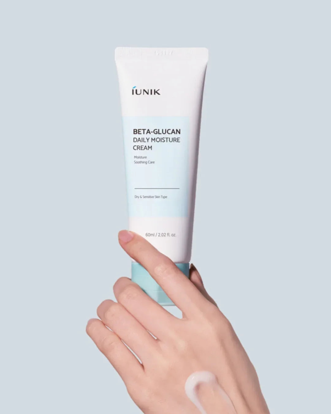 Hand holding iUNIK Beta-Glucan Daily Moisture Cream tube with cream on skin on light blue background