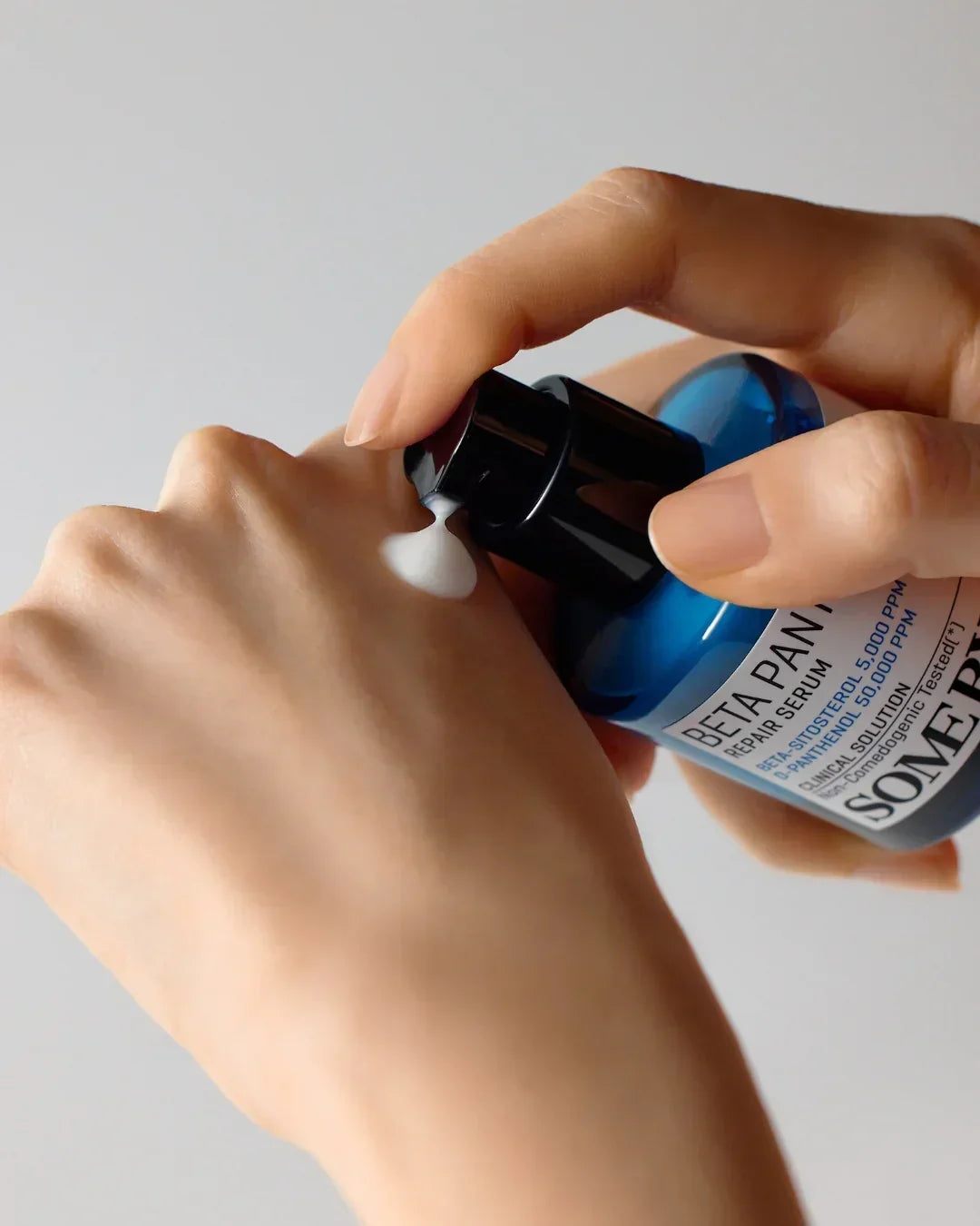 Person applying Beta Panthenol Repair Serum cream from blue bottle onto hand with light background