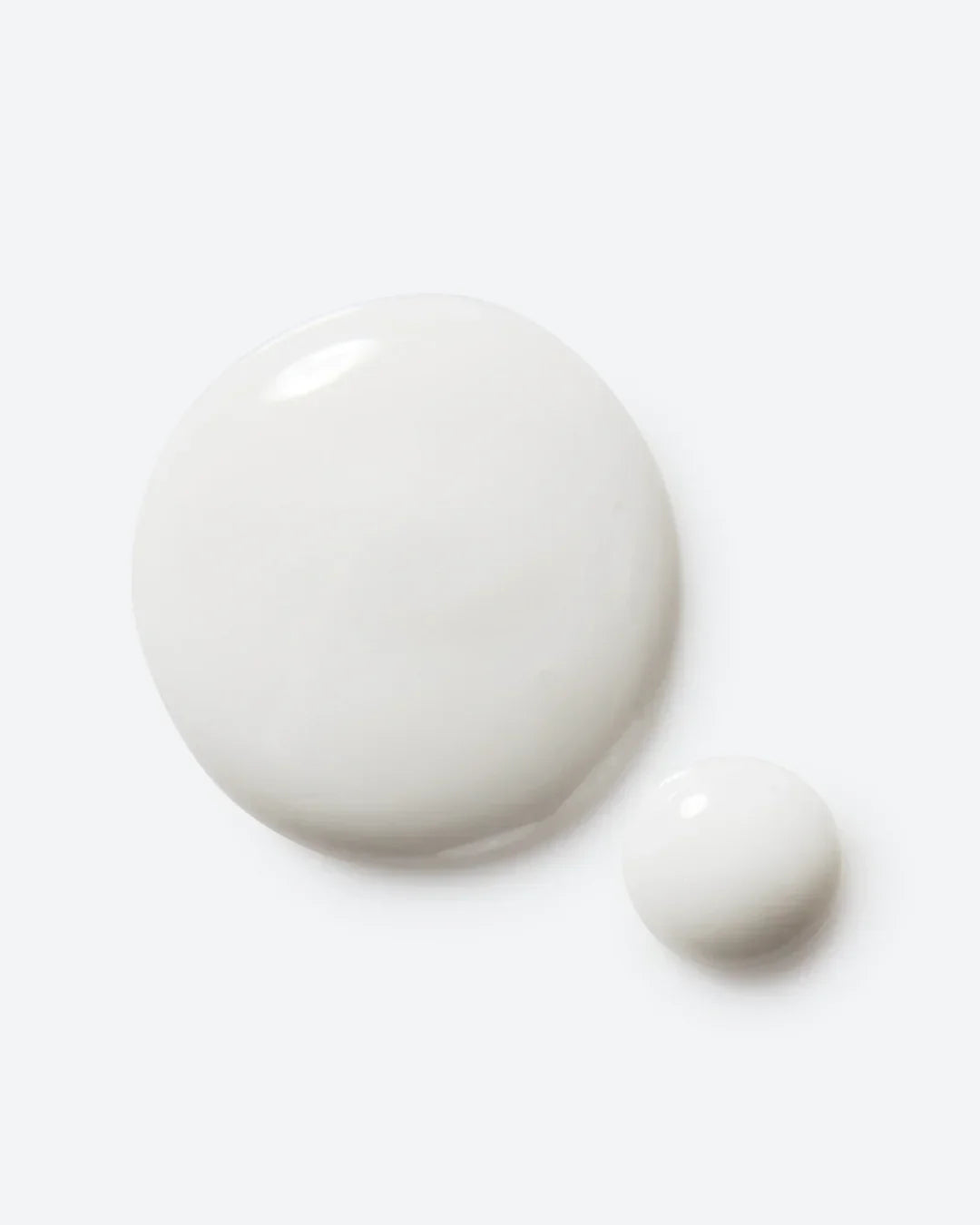 Two drops of smooth white skincare serum texture on a light background