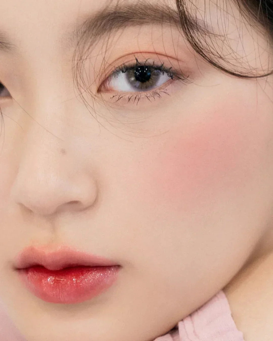 Close-up of a woman's face with natural makeup, pink blush, and glossy pink lips