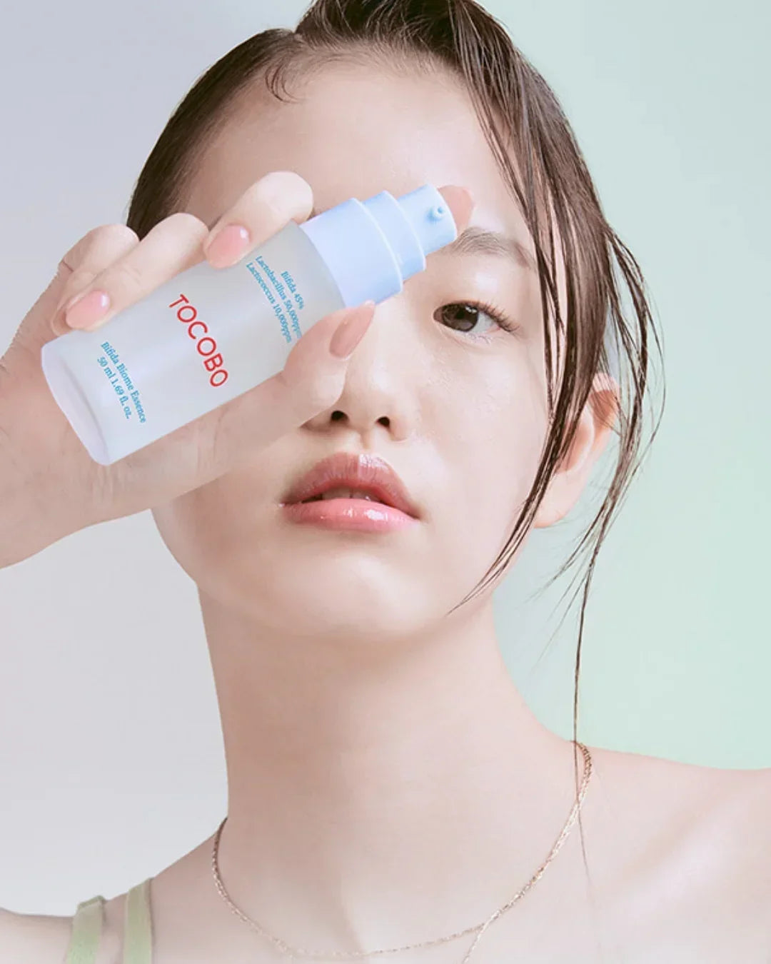 Woman holding Tocobo Bifida Biome Essence skincare product with clear glowing skin