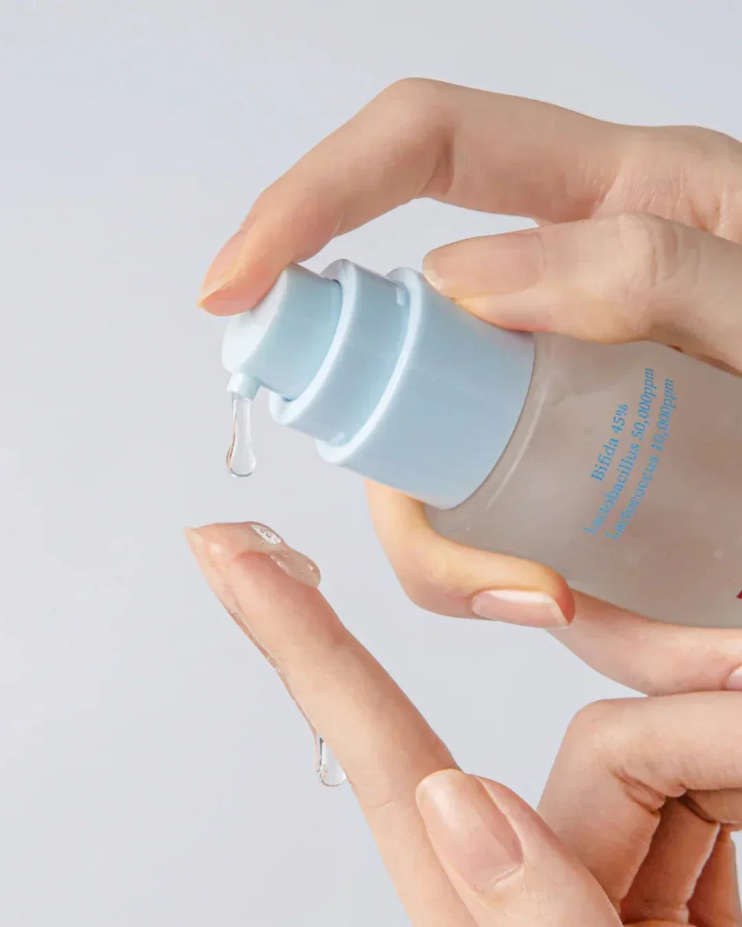 Hand dispensing clear gel serum from pump bottle labeled with bifida and lactobacillus ingredients