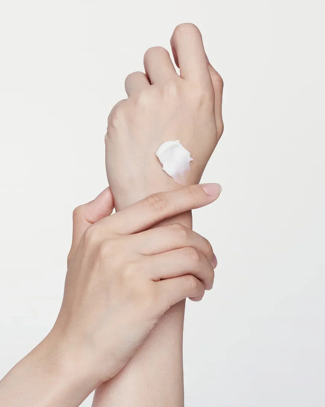 Close-up of hands applying white skincare cream on clean skin with a plain white background