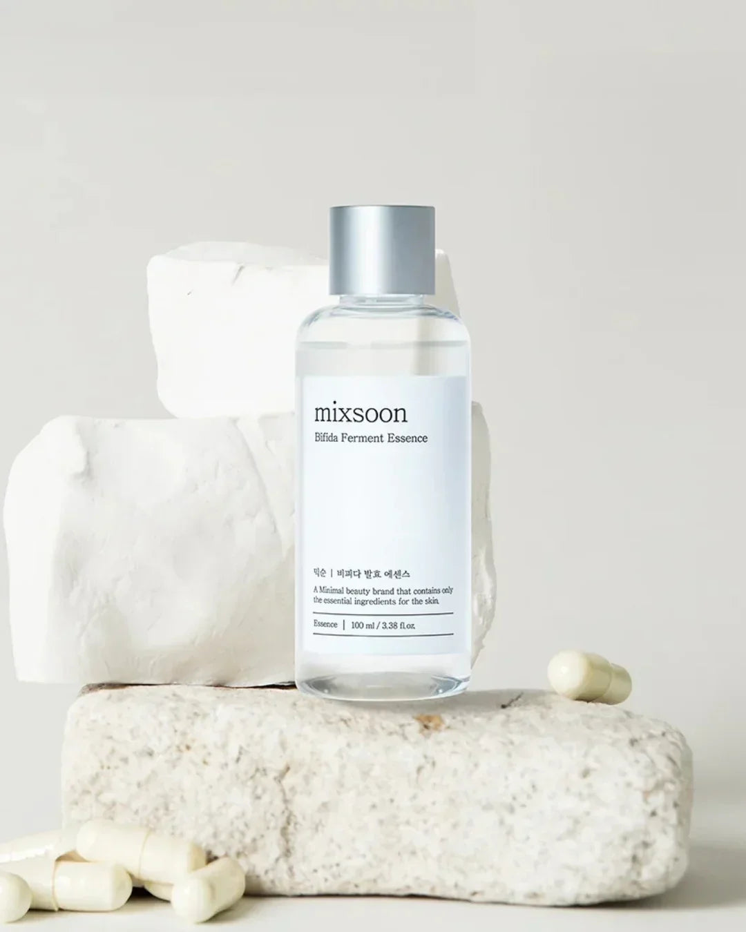 Mixsoon Bifida Ferment Essence bottle on white textured stones with white capsules around