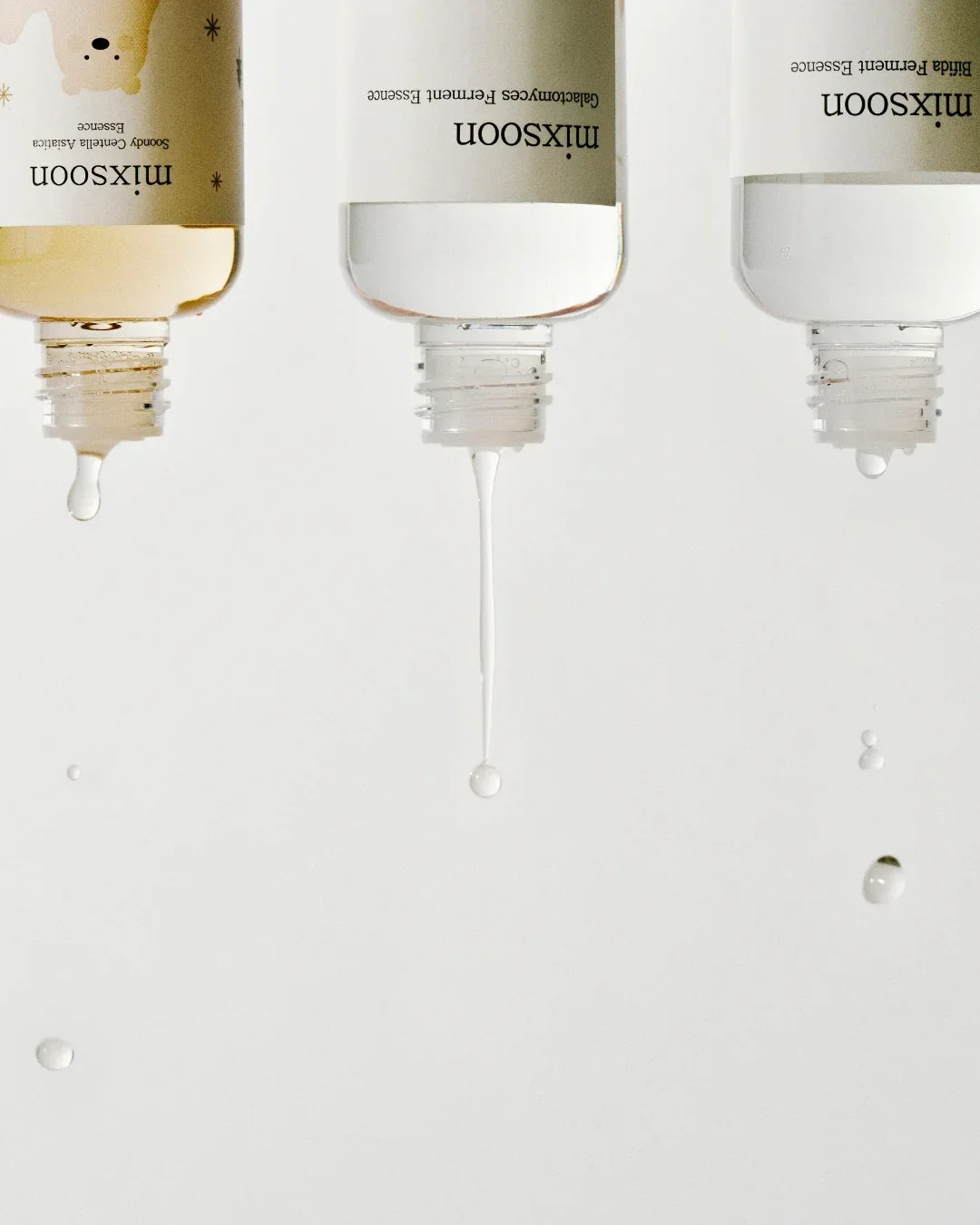 Three upside-down Mixsoon skincare essence bottles dripping liquid on white background