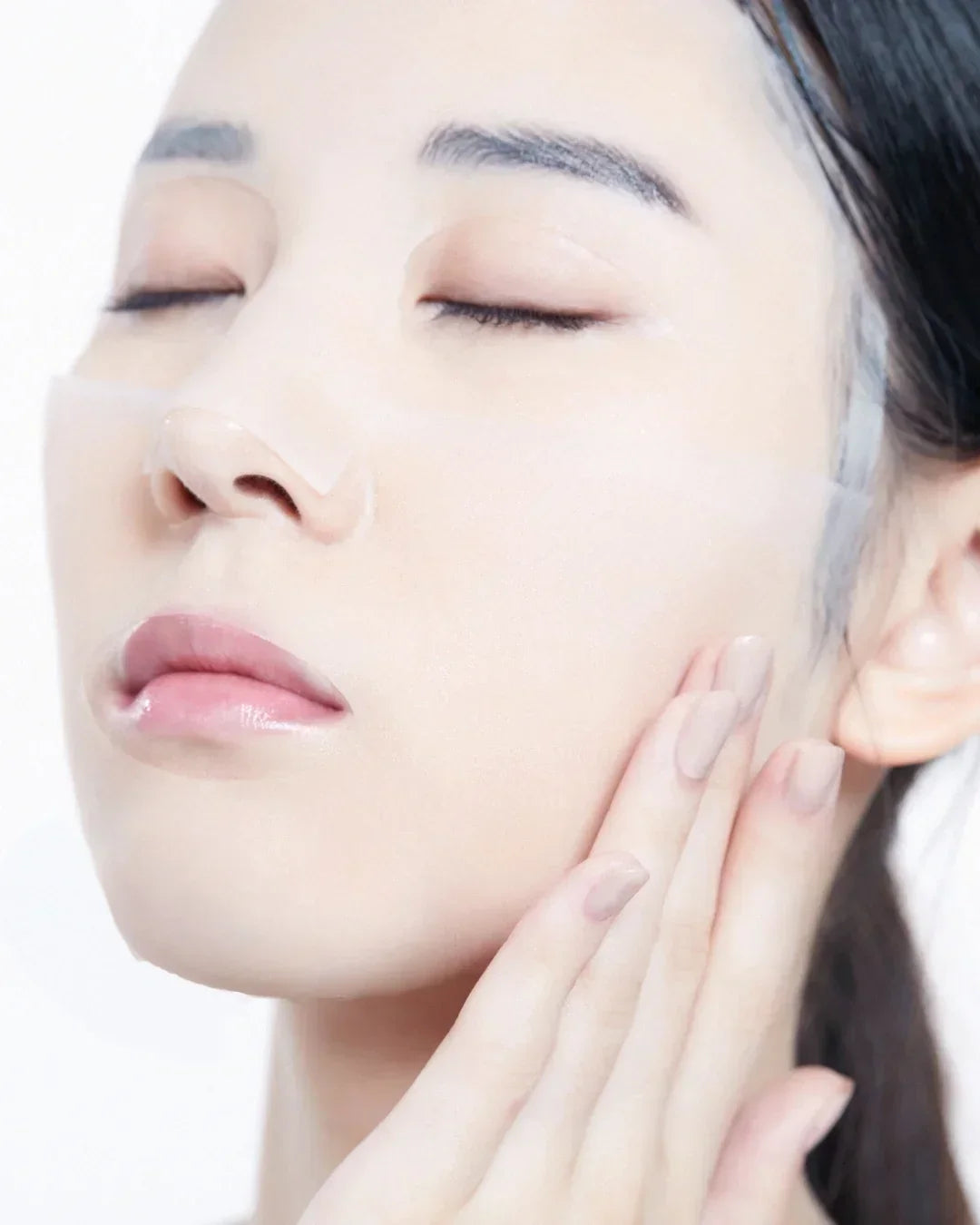 Close-up of woman with closed eyes applying transparent bifida skincare mask on face