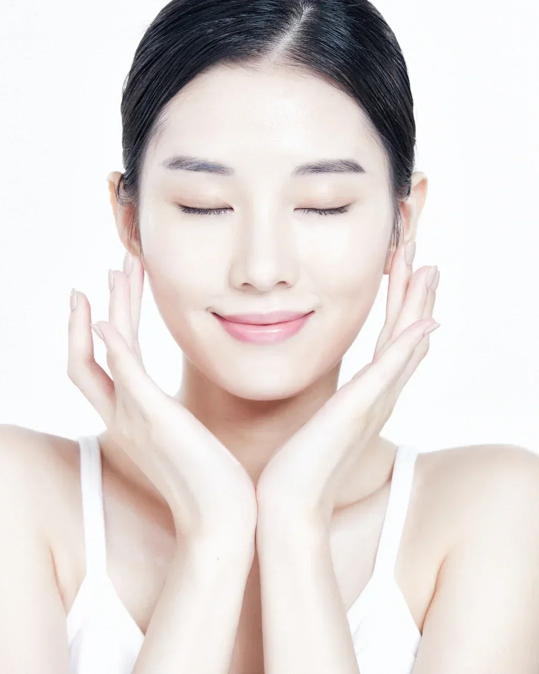 Close-up of a woman with clear glowing skin gently touching her face, eyes closed, smiling softly