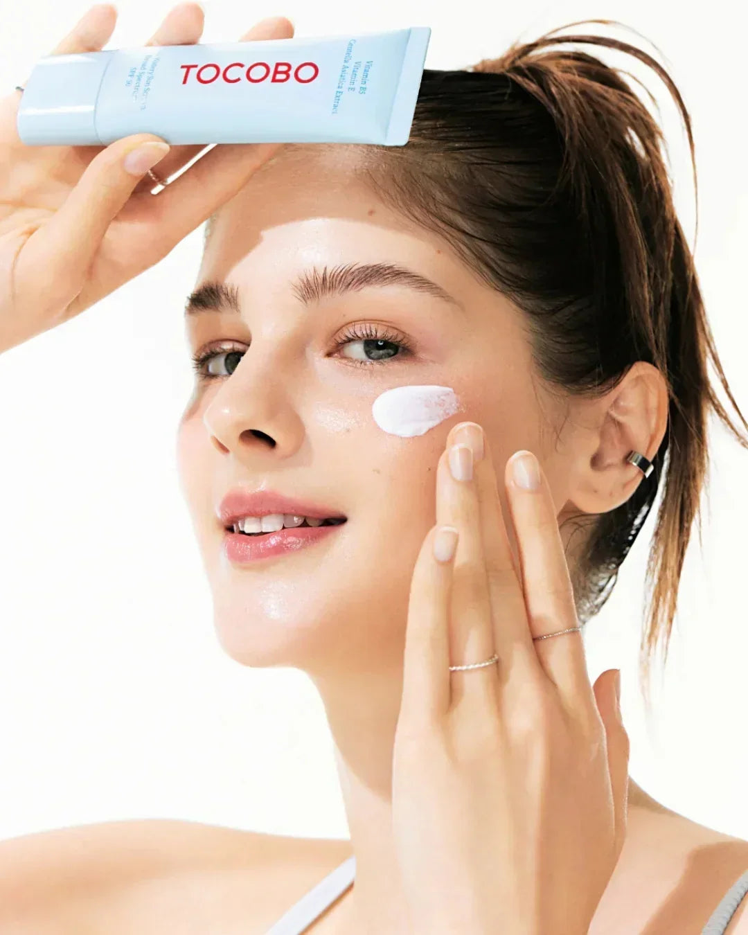 Woman applying TOCOBO SPF50 PA waterproof sun cream on face with clear, glowing skin