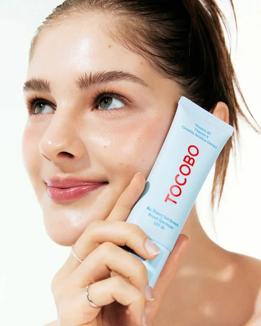 Smiling woman holding TOCOBO Bio Watery Sun Screen SPF 50 with clear glowing skin