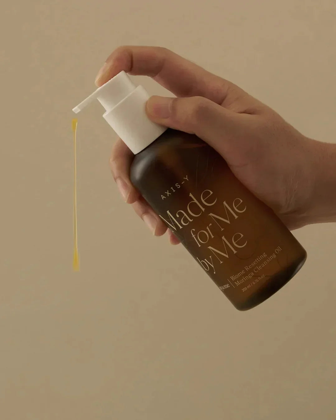 Hand holding Axis-Y Made for Me by Me Biome Resetting Moringa Cleansing Oil with yellow oil drop