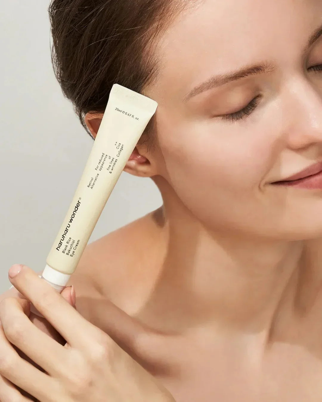 Close-up of woman holding Naruko Black Rice Bakuchiol eye cream tube near her face with closed eyes